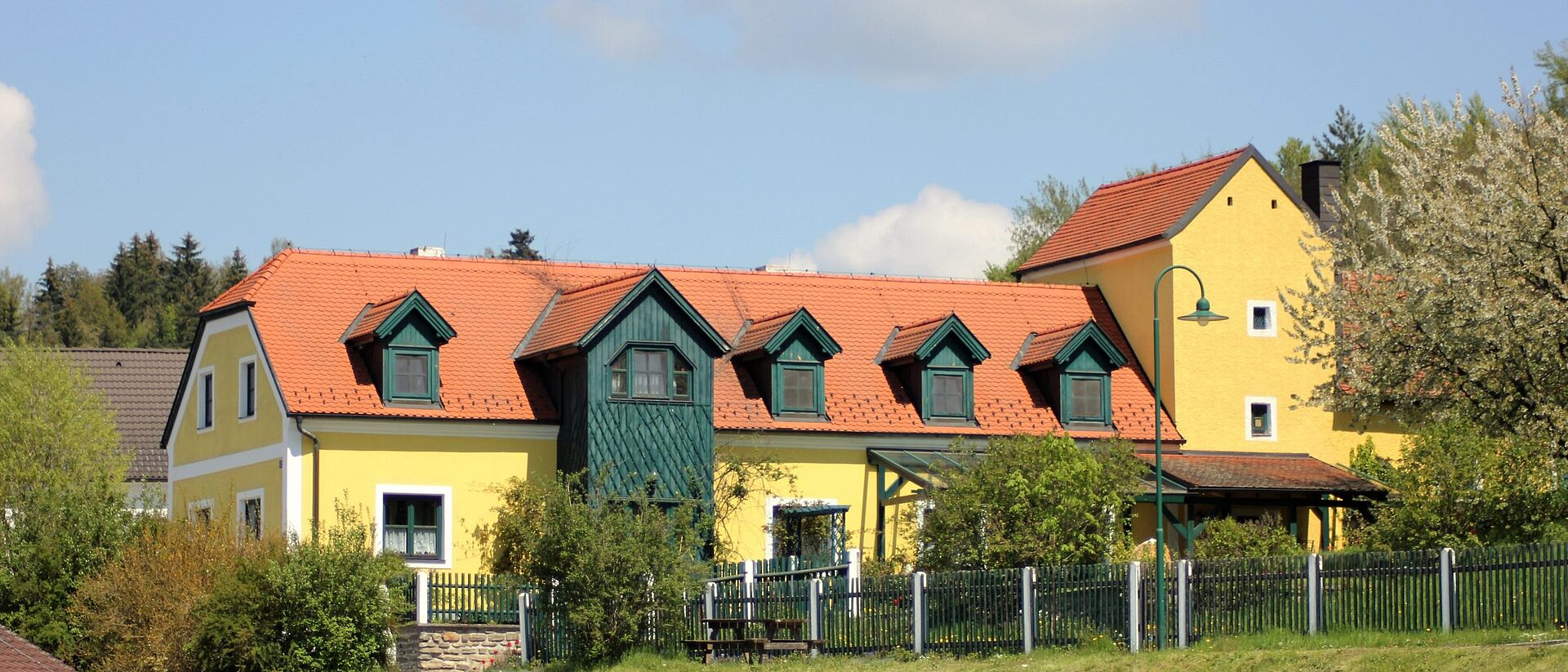 Das alte Forsthaus in Messern: gelbes Haus mit rotem Dach und grünen Fensterläden vor blauem Himmel